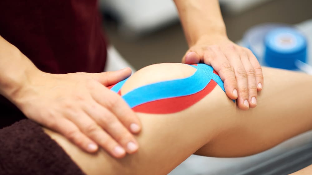 Sports injury kinesio treatment — therapist placing kinesio tape on patient's knee